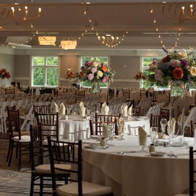 Elegant banquet hall set up with tables, floral centerpieces, and warm lighting.