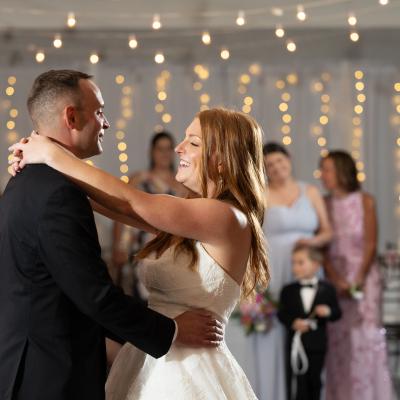 A couple dances joyfully at their wedding, surrounded by guests and twinkling lights.