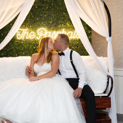 A newlywed couple kisses on a cozy bench with a decorative backdrop.