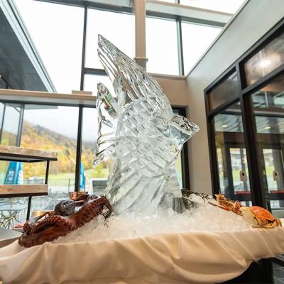 Ice sculpture of a fish displays seafood on a white table with windows in the background.