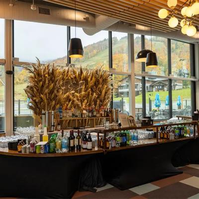 Modern bar with a variety of drinks, large windows, and autumn scenery outside.