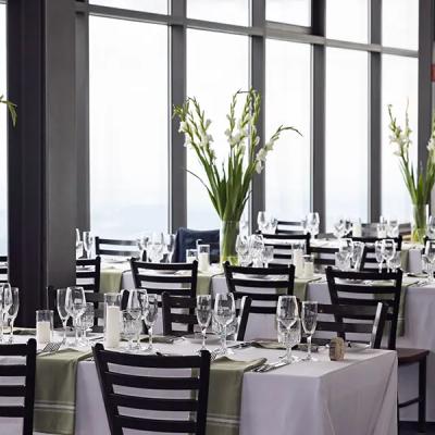 Elegant dining setup with white tables, glassware, and floral arrangements by large windows.