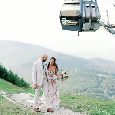 Couple in wedding attire poses on a mountaintop with a gondola in the background.
