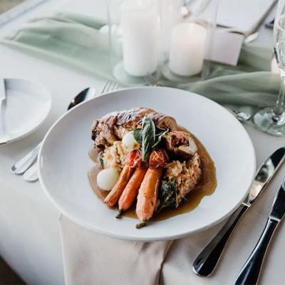 A plated gourmet dish with meat, vegetables, and garnishes on a dining table.