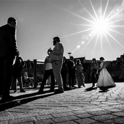 A wedding scene in black and white, with guests and a bride under a bright sun.