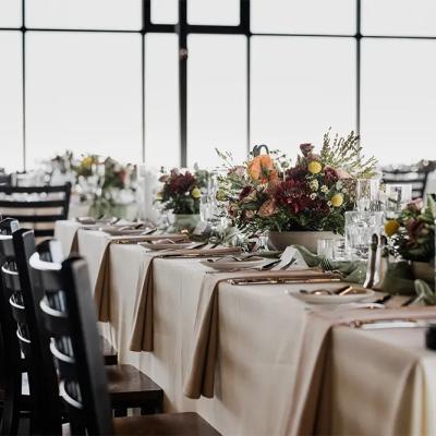 Elegant dining setup with floral arrangements and glassware, against large windows.