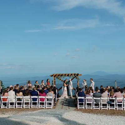 A scenic outdoor wedding ceremony with guests and mountains in the background.