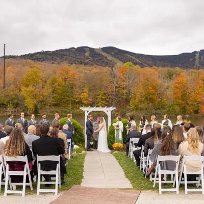 A wedding ceremony by a lake, surrounded by colorful autumn foliage and mountains.