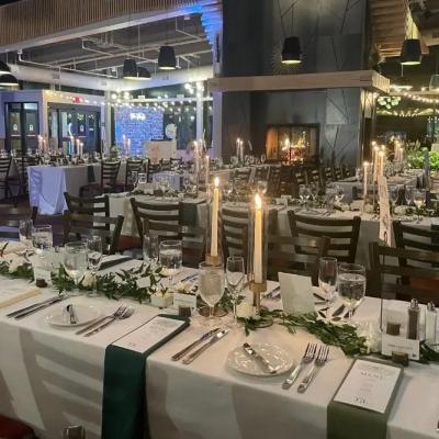 Elegant dining setup with tables, candles, and greenery in a softly lit venue.