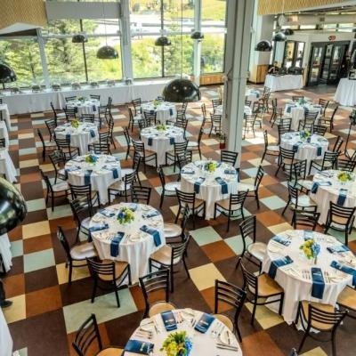 Spacious dining hall set for an event, featuring round tables with floral centerpieces.