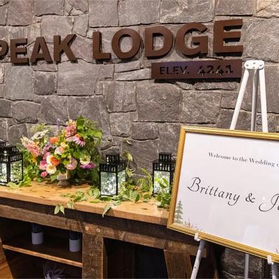 Wedding welcome sign for Brittany and John at Peak Lodge, adorned with flowers and lanterns.