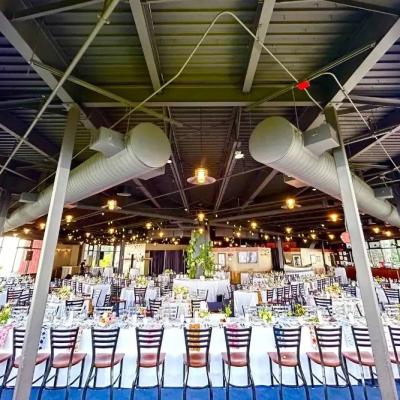 Elegant dining setup in a large, modern venue with string lights and floral centerpieces.