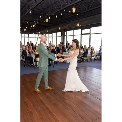 Couple dances on a wooden floor, surrounded by guests at a wedding reception.
