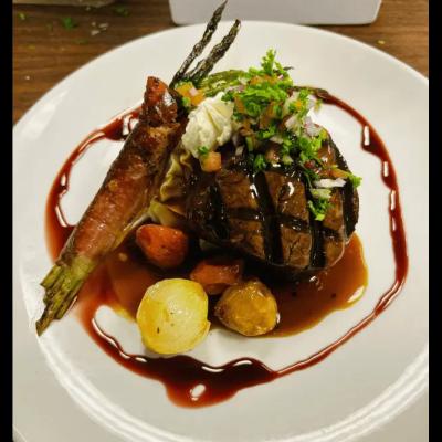 Grilled steak with vegetables, mashed potato, and a red sauce drizzle, garnished with herbs.