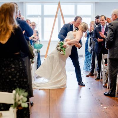 A couple shares a kiss while guests applaud during their wedding ceremony.
