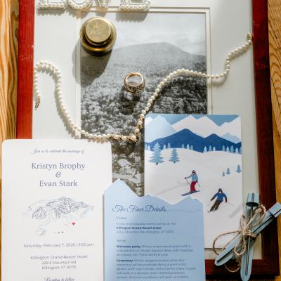Wedding invitation details, rings, and decorative elements on a wooden table.
