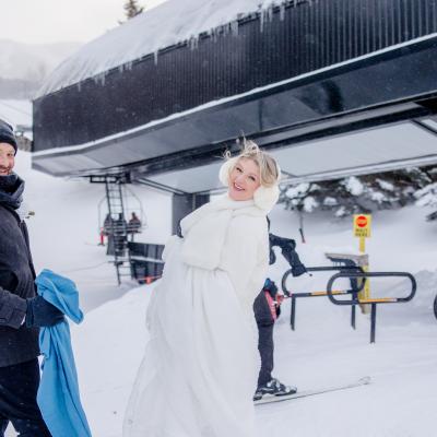 Couple in winter attire smiles near a ski lift in snowy mountains.