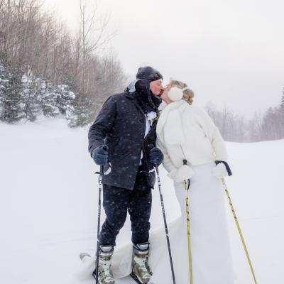 A couple in winter attire shares a kiss while skiing in a snowy landscape.