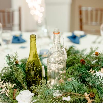 Two bottles on a green garland centerpiece at a festive table setting.