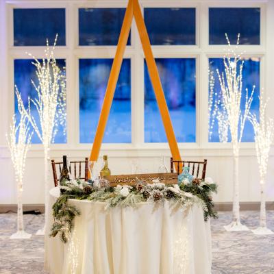Decorated wedding table with lights, greenery, and a name sign, set against a window backdrop.