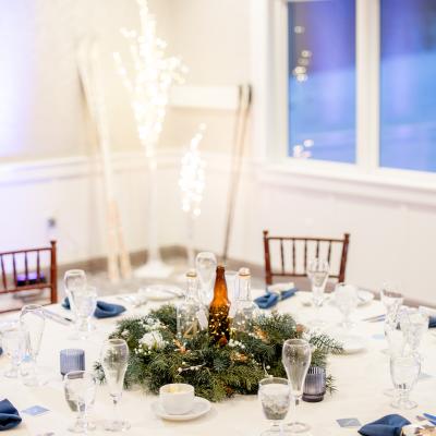 Elegant dining table with glassware, a greenery centerpiece, and festive lighting.