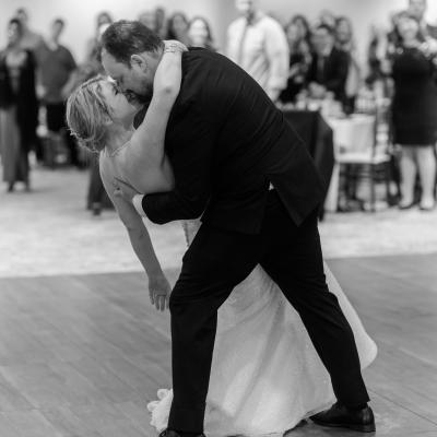 A couple shares a romantic dance, leaning in for a kiss, surrounded by guests.