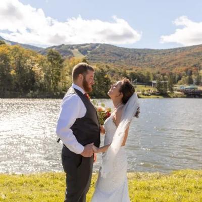 A happy couple exchanges vows by a shimmering lake in a scenic, autumn landscape.