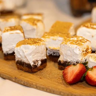 Sliced dessert bars with toasted meringue and strawberries on a wooden platter.