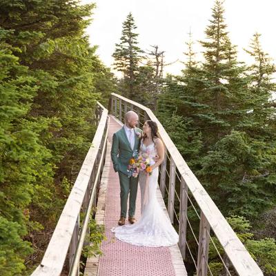 A newlywed couple stands on a wooden walkway surrounded by lush greenery.