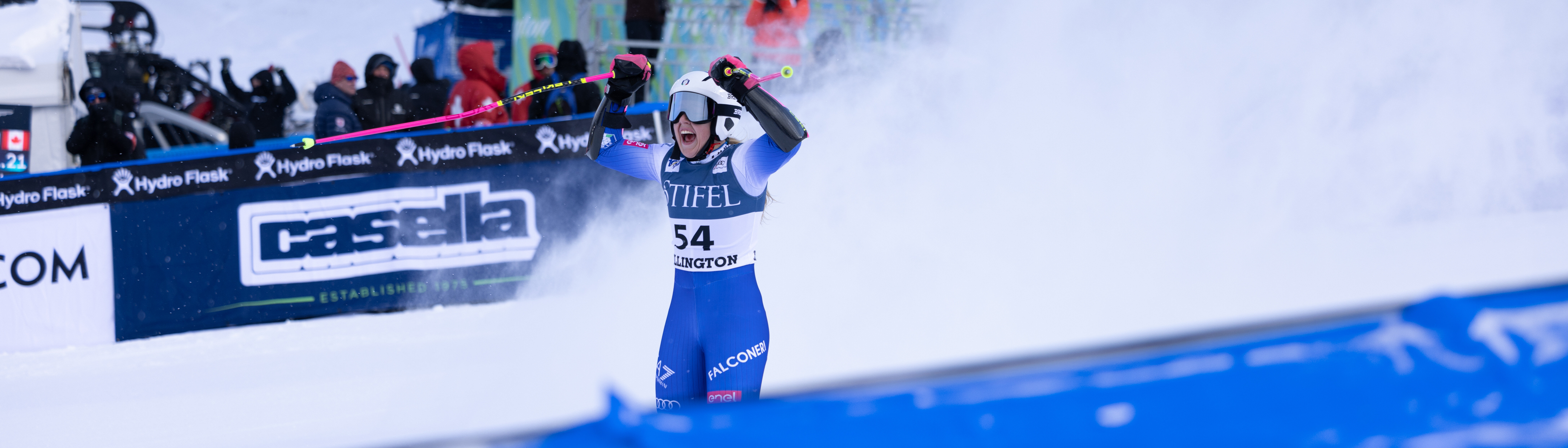 A skier celebrates with raised arms on a snowy slope, surrounded by spectators.