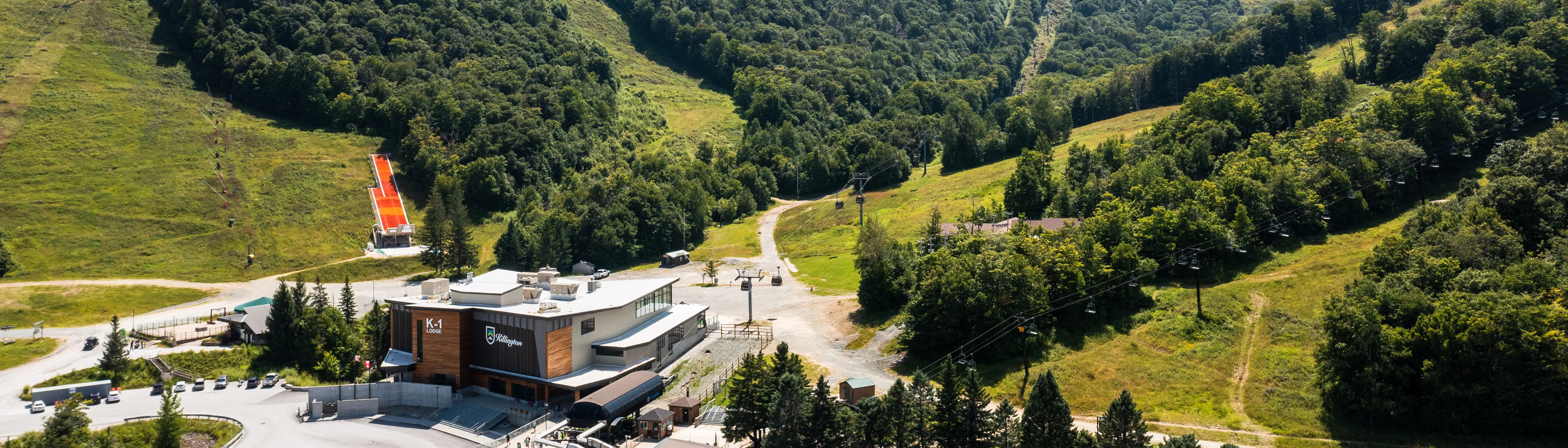 Aerial view of a ski resort with green hills and a lodge in the foreground.