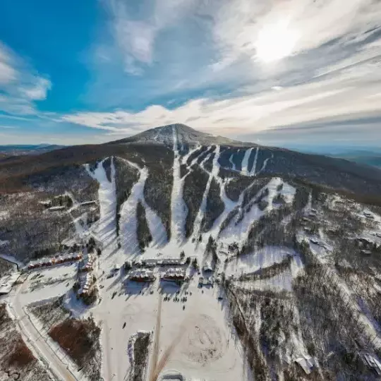 Aerial view of a snow-covered mountain with ski slopes and a lodge at the base.