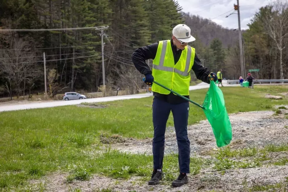 Person in a neon vest picking up litter along a roadside.