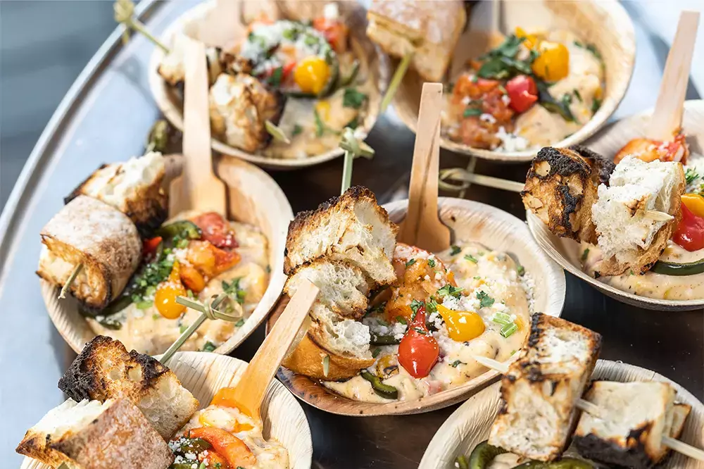 Bowls of creamy dish topped with vegetables and pieces of toasted bread on a serving tray.
