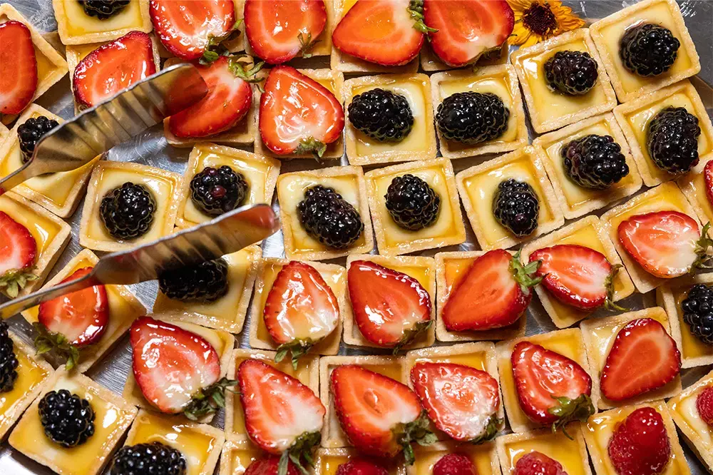 Tiny tart desserts topped with strawberries and blackberries on a silver platter.