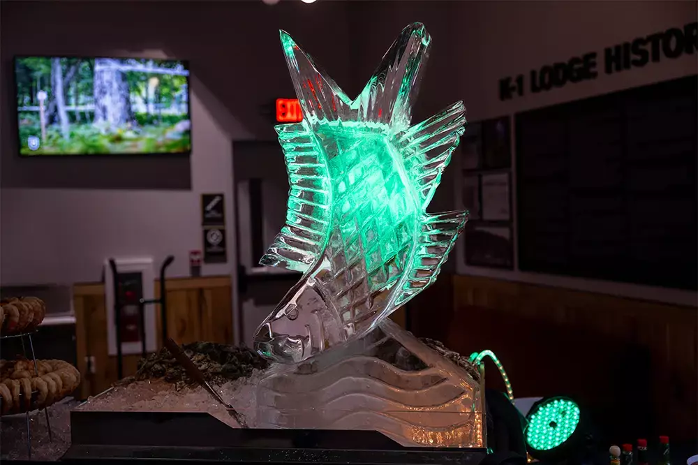 Illuminated ice sculpture of a fish on display in a lodge setting.