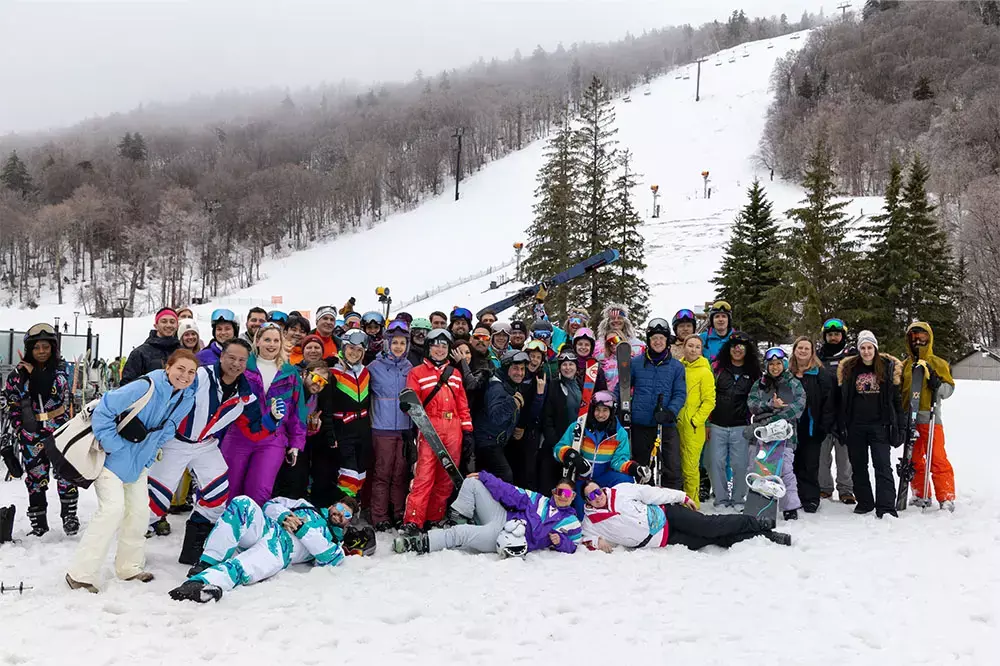 A large group of people in colorful ski attire poses together on a snowy hillside.