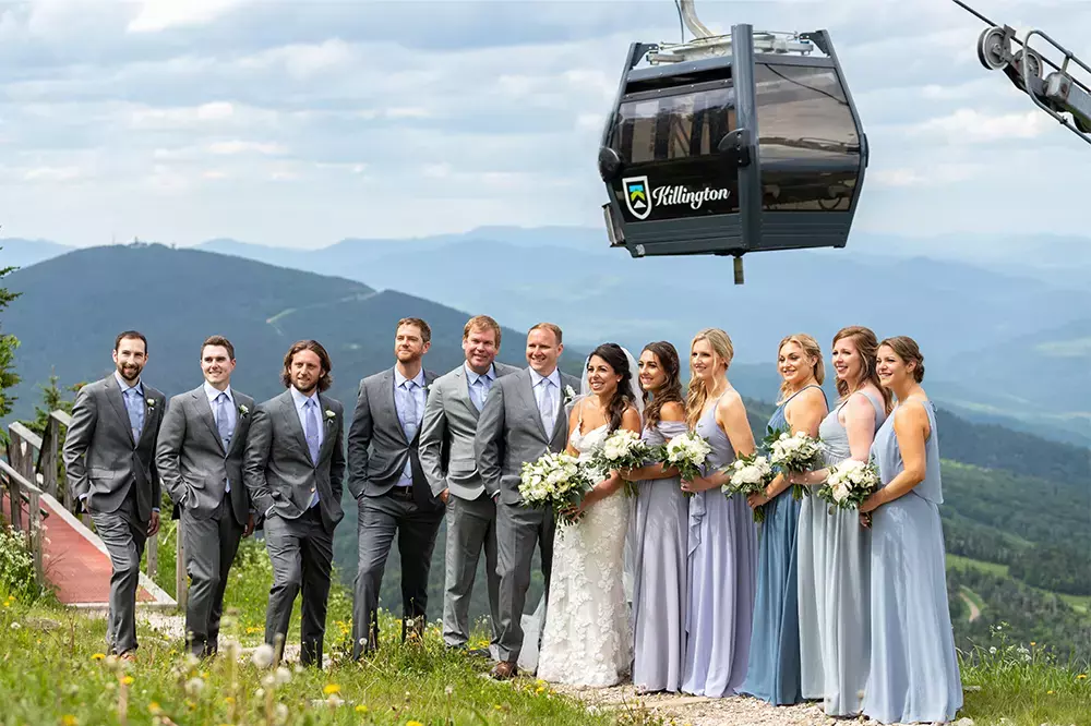 Wedding party poses outdoors with mountains in the background and a gondola above.