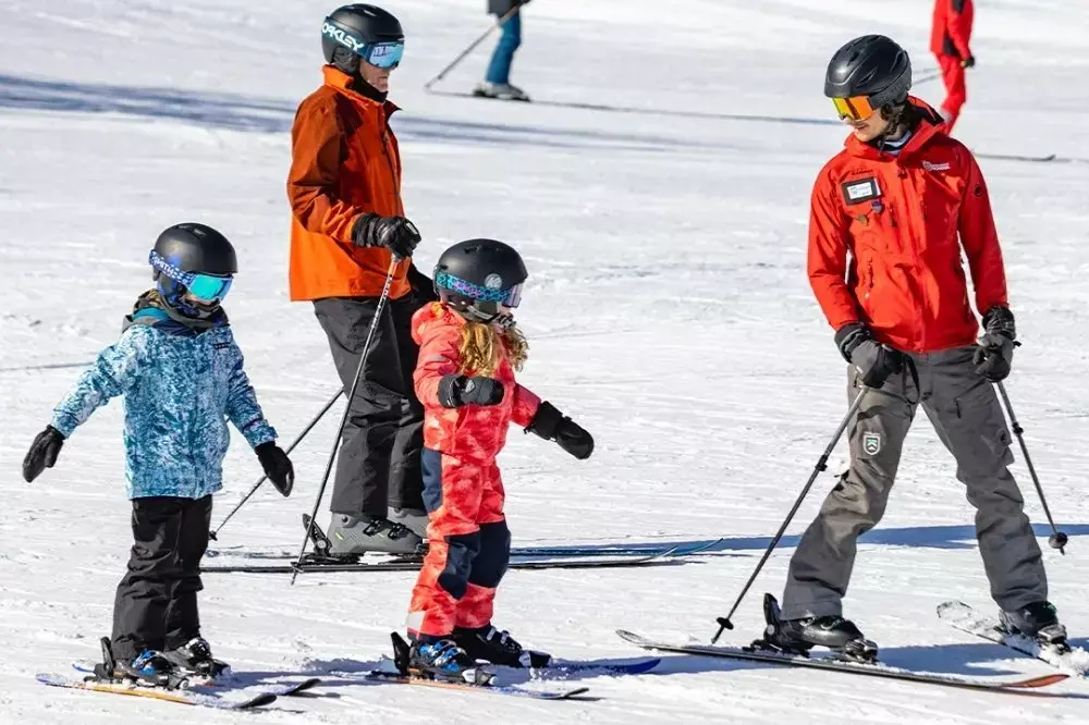 Two children ski with an instructor on snow-covered slopes.