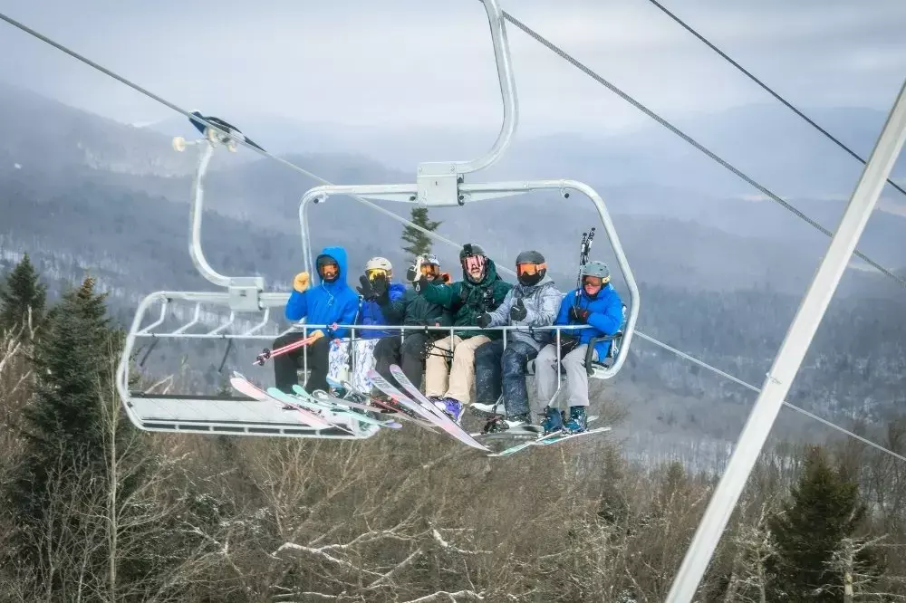 Six skiers riding a chairlift in a snowy mountain landscape.