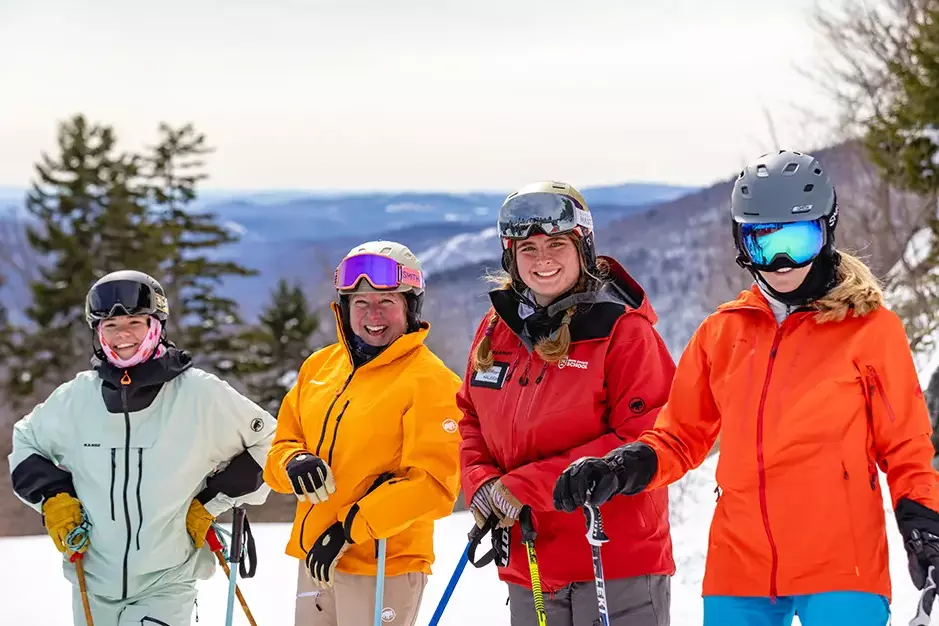 Four skiers smiling at the camera, dressed in colorful ski gear on a snowy mountain.
