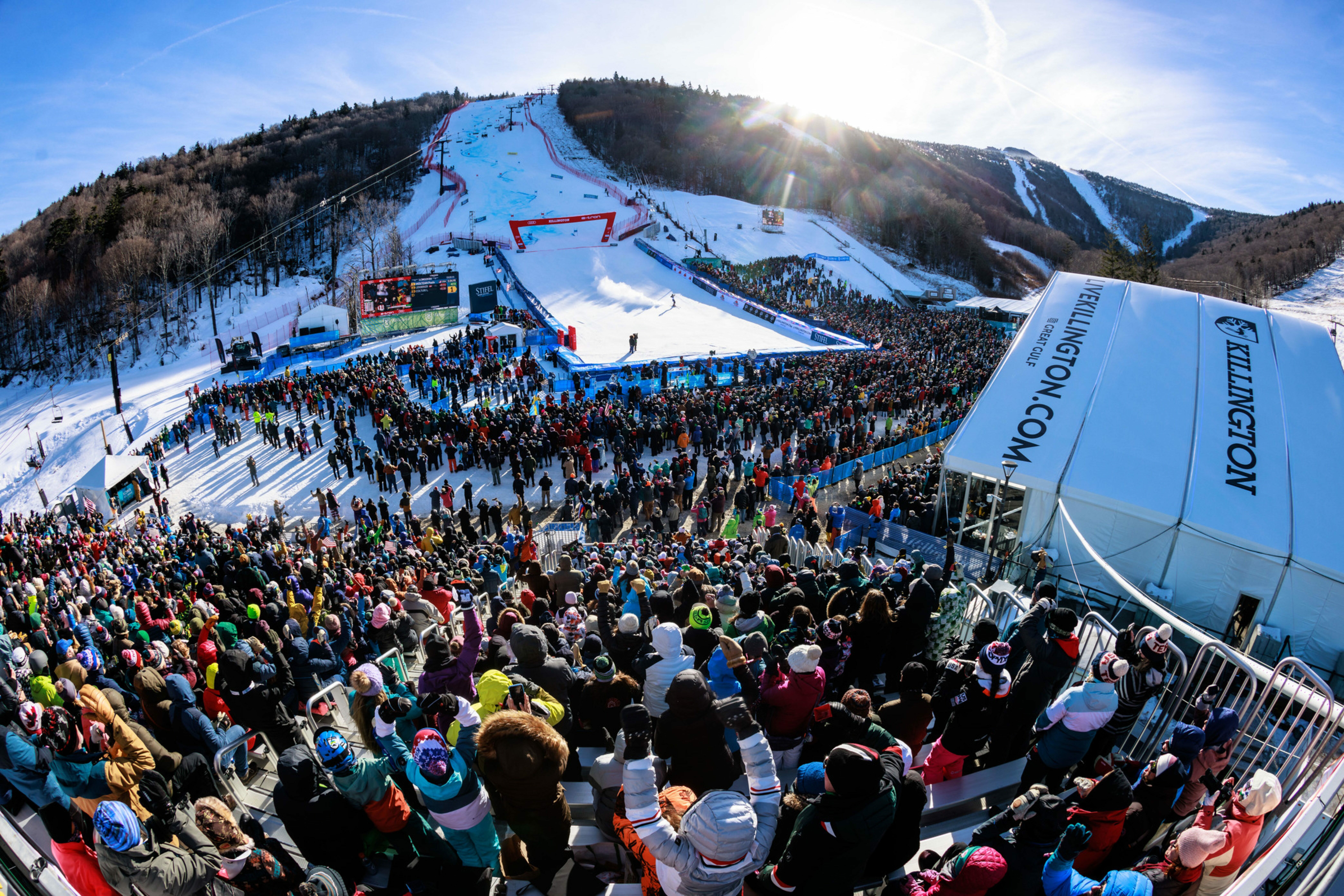 Crowd watching a ski competition on a snowy mountain with vibrant blue skies.