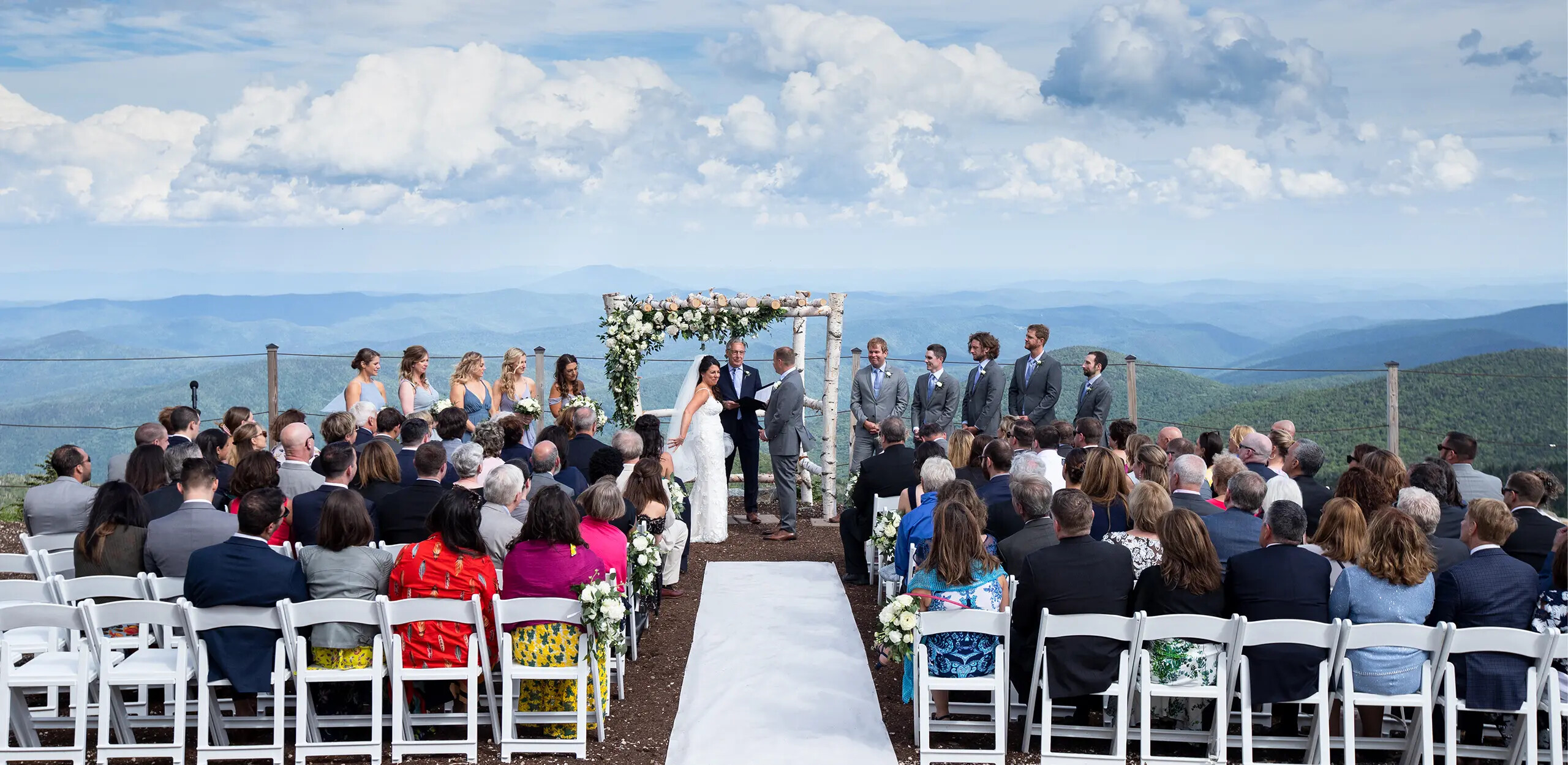 Outdoor wedding ceremony on a mountain with guests and scenic views in the background.