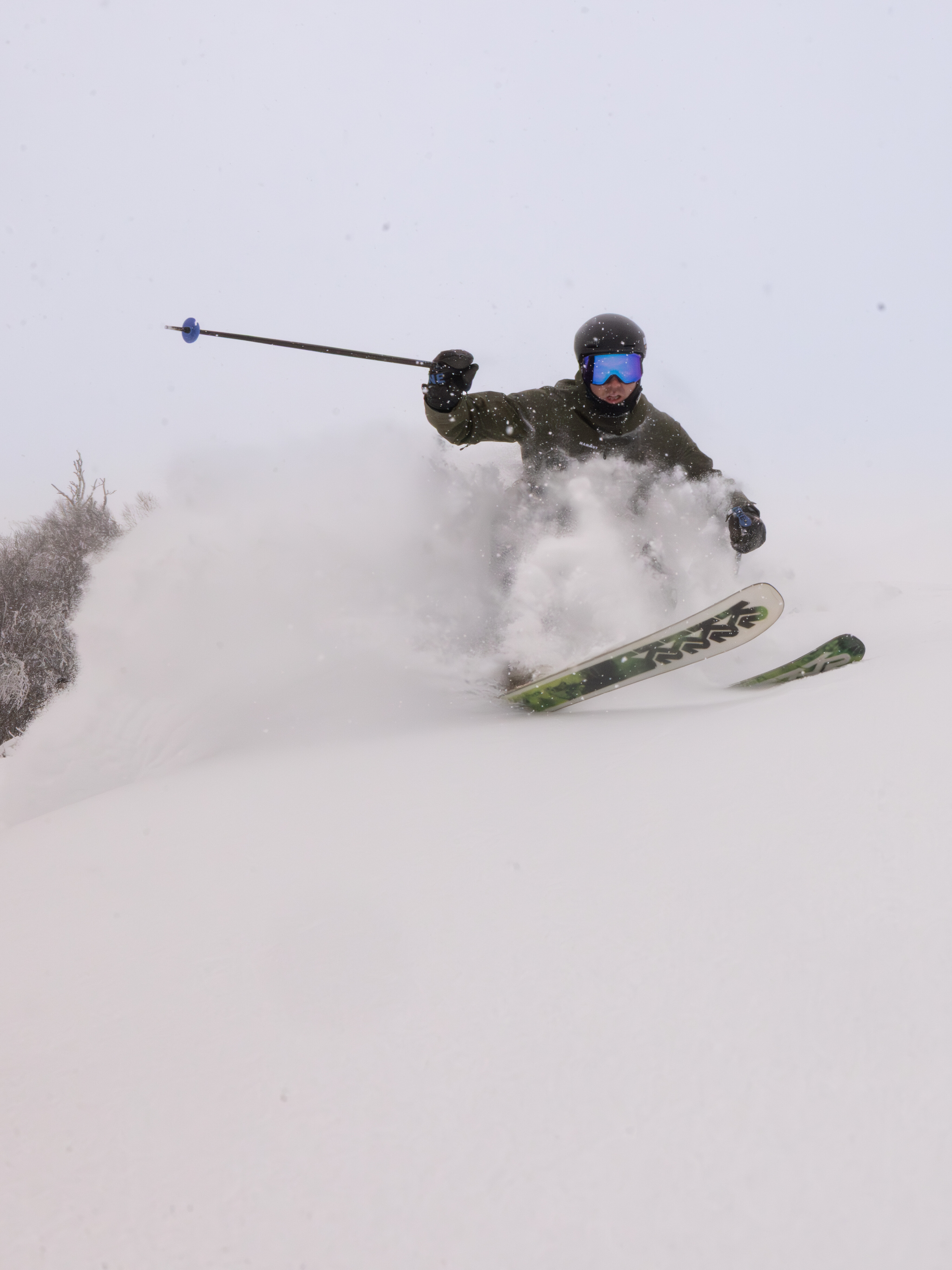 A skier carves through deep snow on a overcast day, with a spray of powder around them.