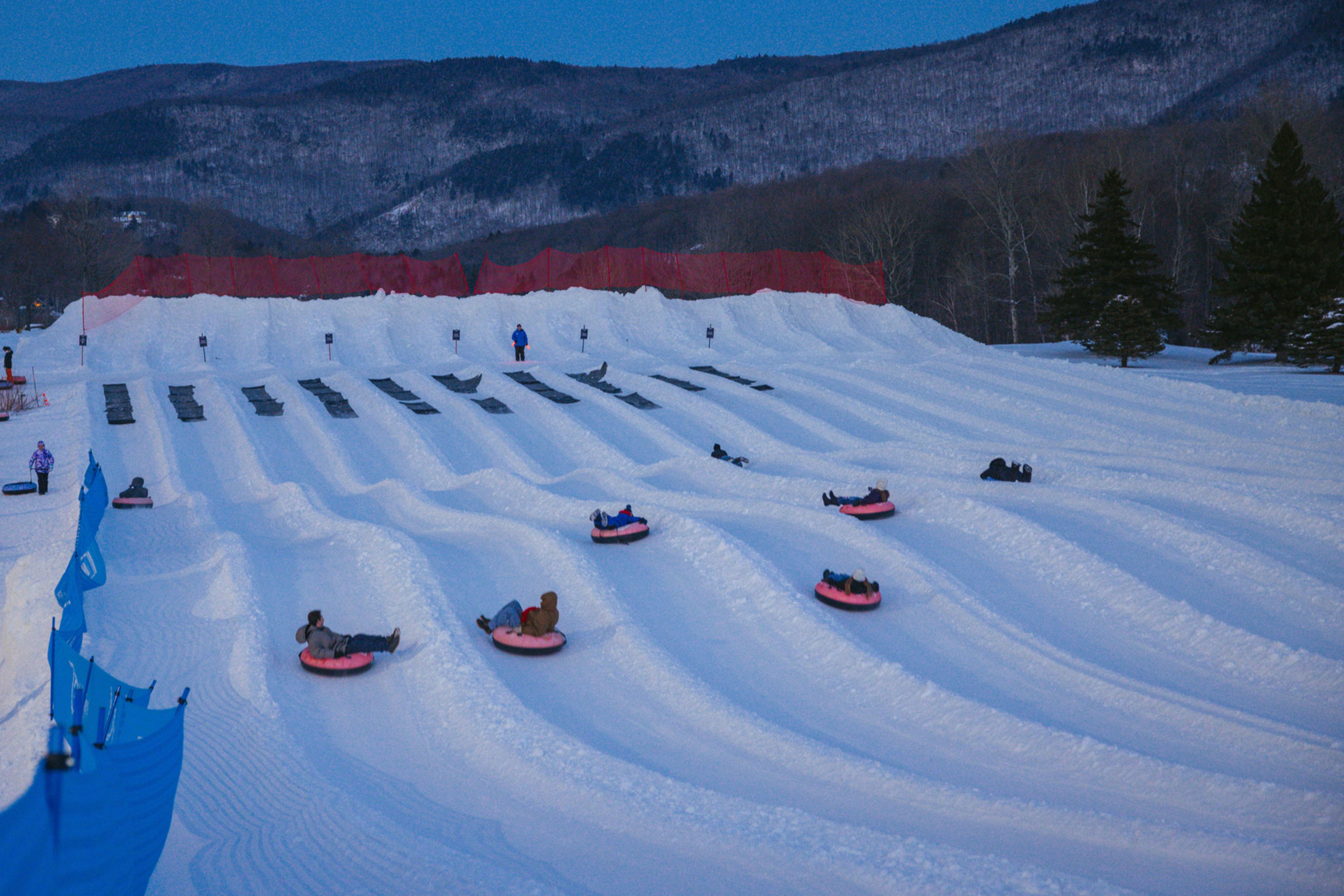 Snow tubing slopes with several people riding tubes in a winter landscape at dusk.