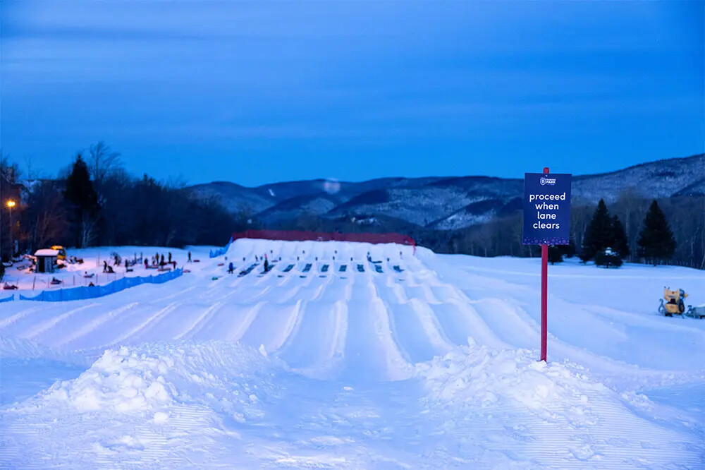Snow tubing lanes with a sign saying "proceed when lane clears" at dusk.