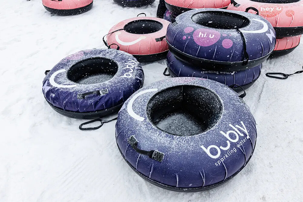 Colorful snow tubes are stacked on snowy ground, some covered in light snow.