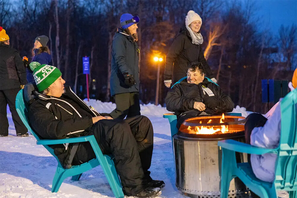 People gather around a fire pit on snow, enjoying the winter evening.