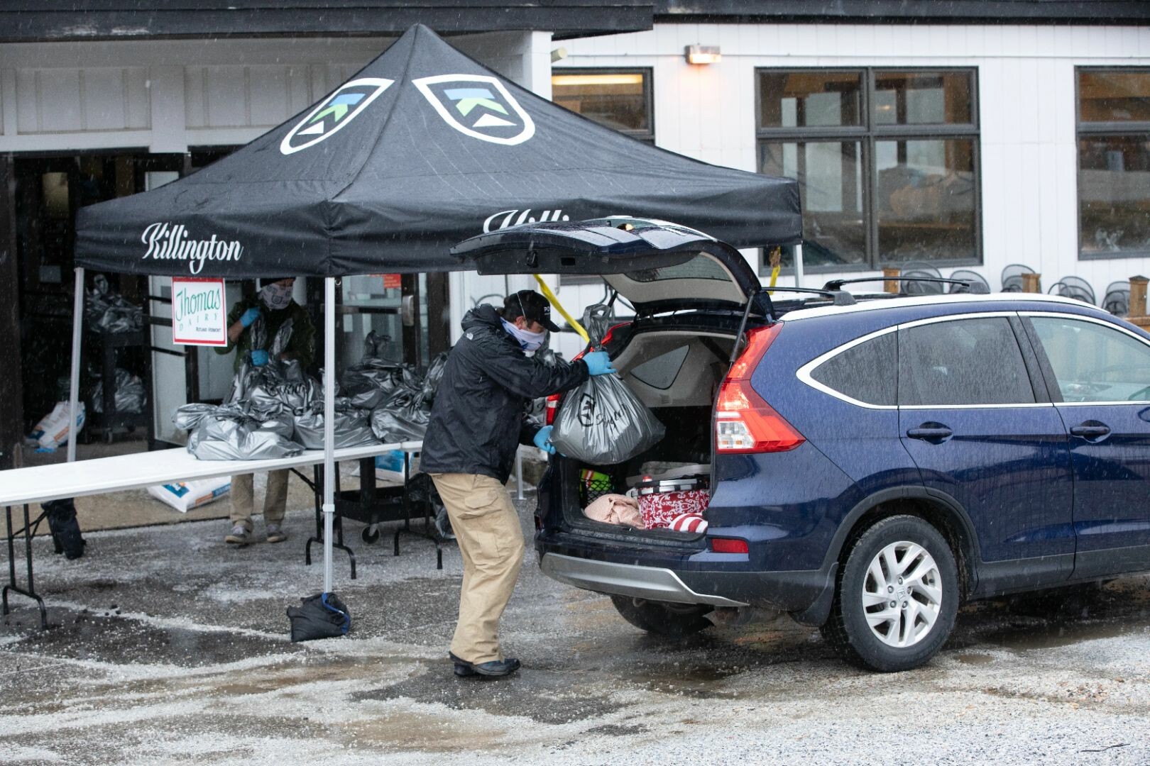 A person loading bags into the trunk of a car at a snowy outdoor distribution event.