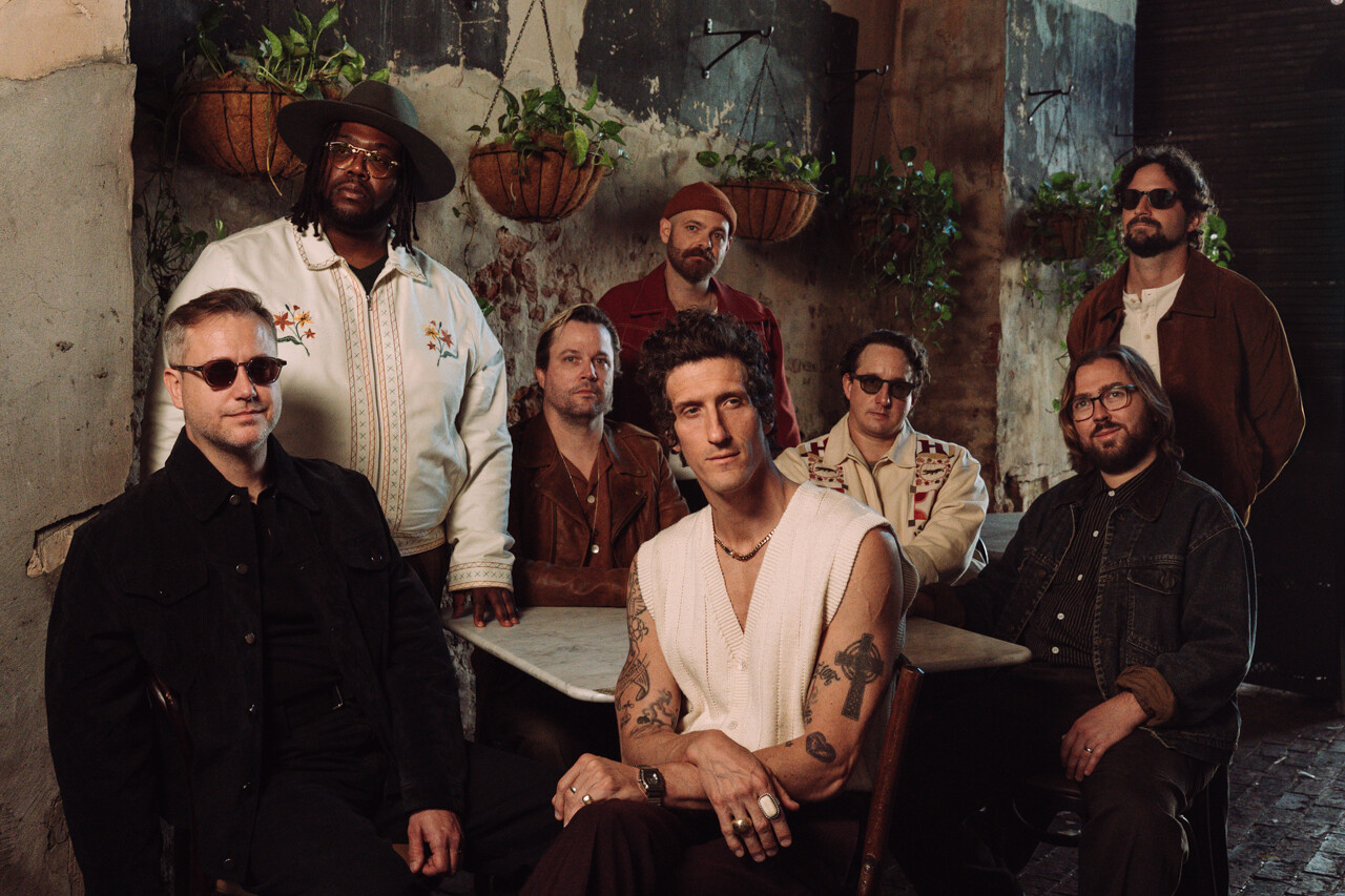 A group of eight men posing together in a rustic indoor setting.